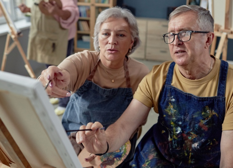 An older couple painting at an easel together.